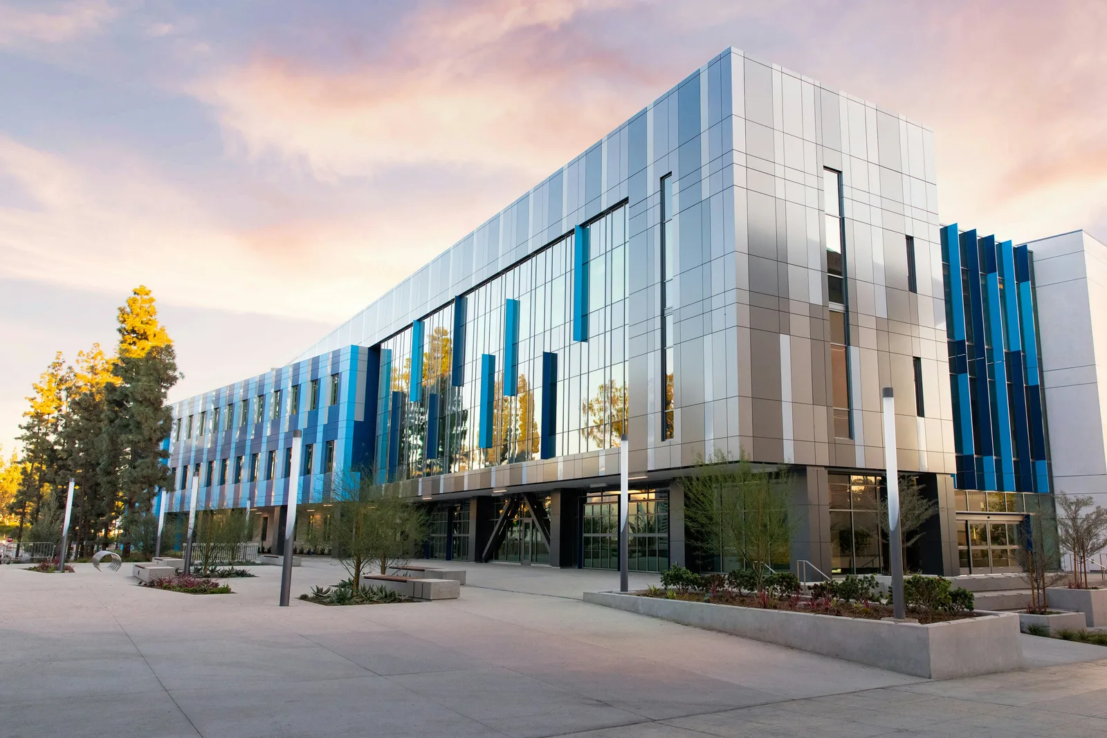 A modern glass and metal academic building at dusk, with an empty plaza in front