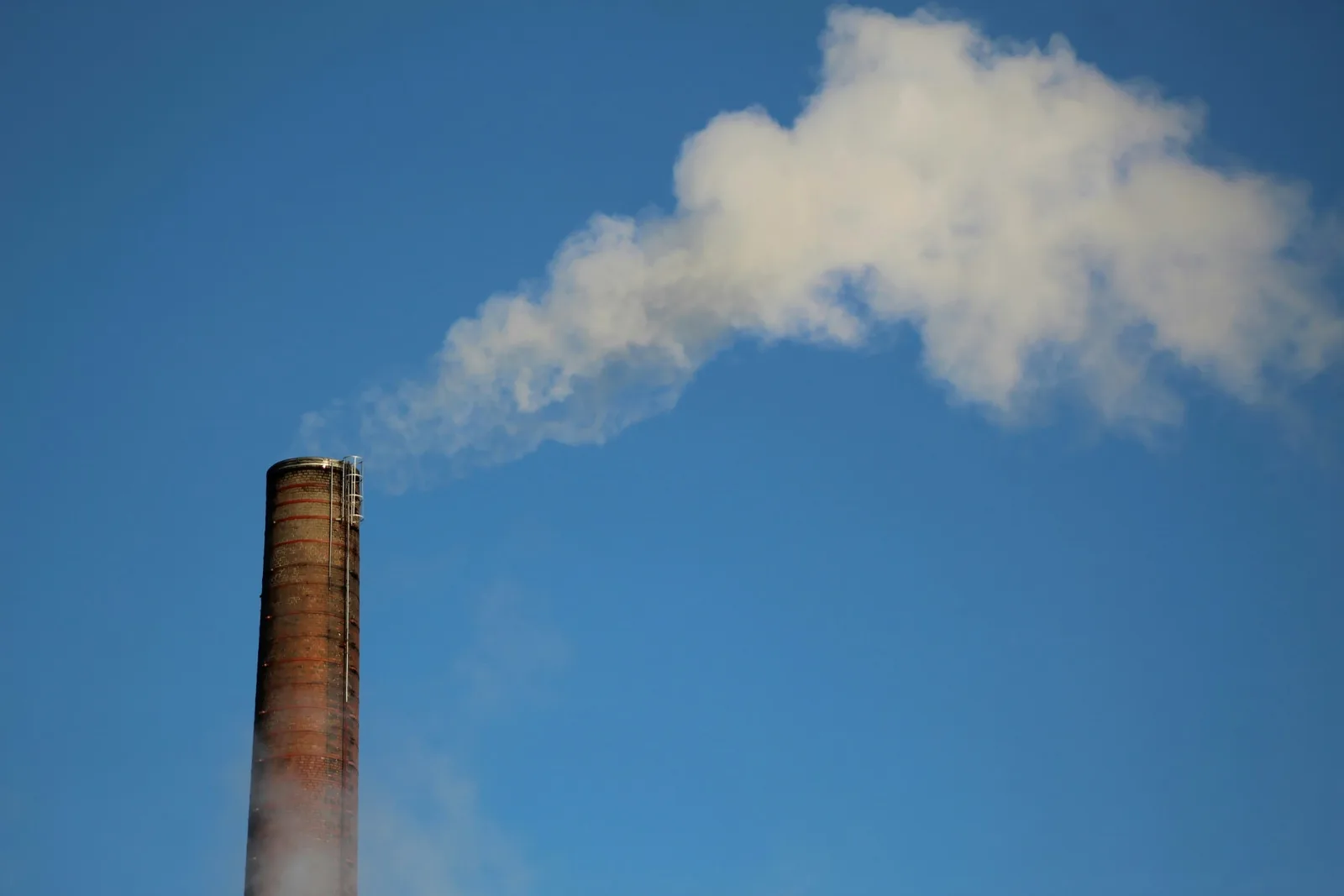 A brick smokestack releasing a white plume into a clear blue sky