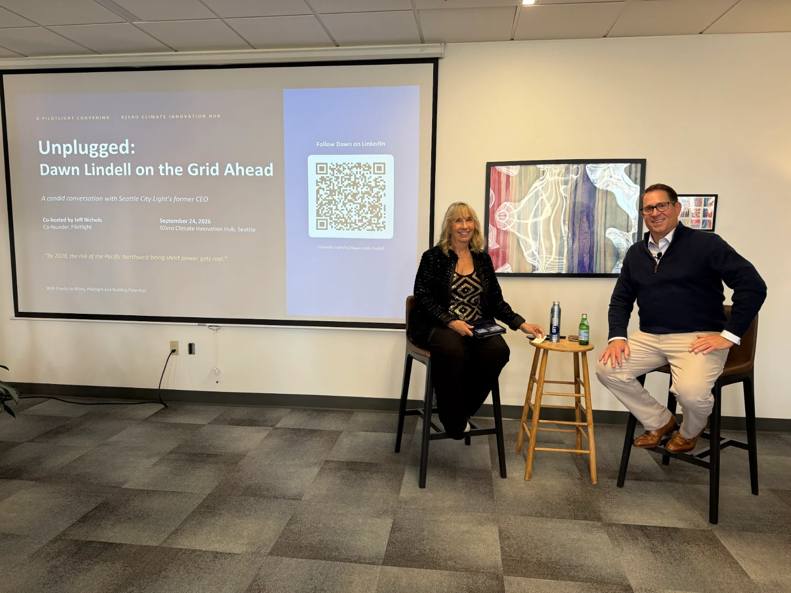 Dawn Lindell and Jeff Nichols seated on stage beside the "Unplugged: Dawn Lindell on the Grid Ahead" title slide at the 9Zero Climate Innovation Hub in Seattle.
