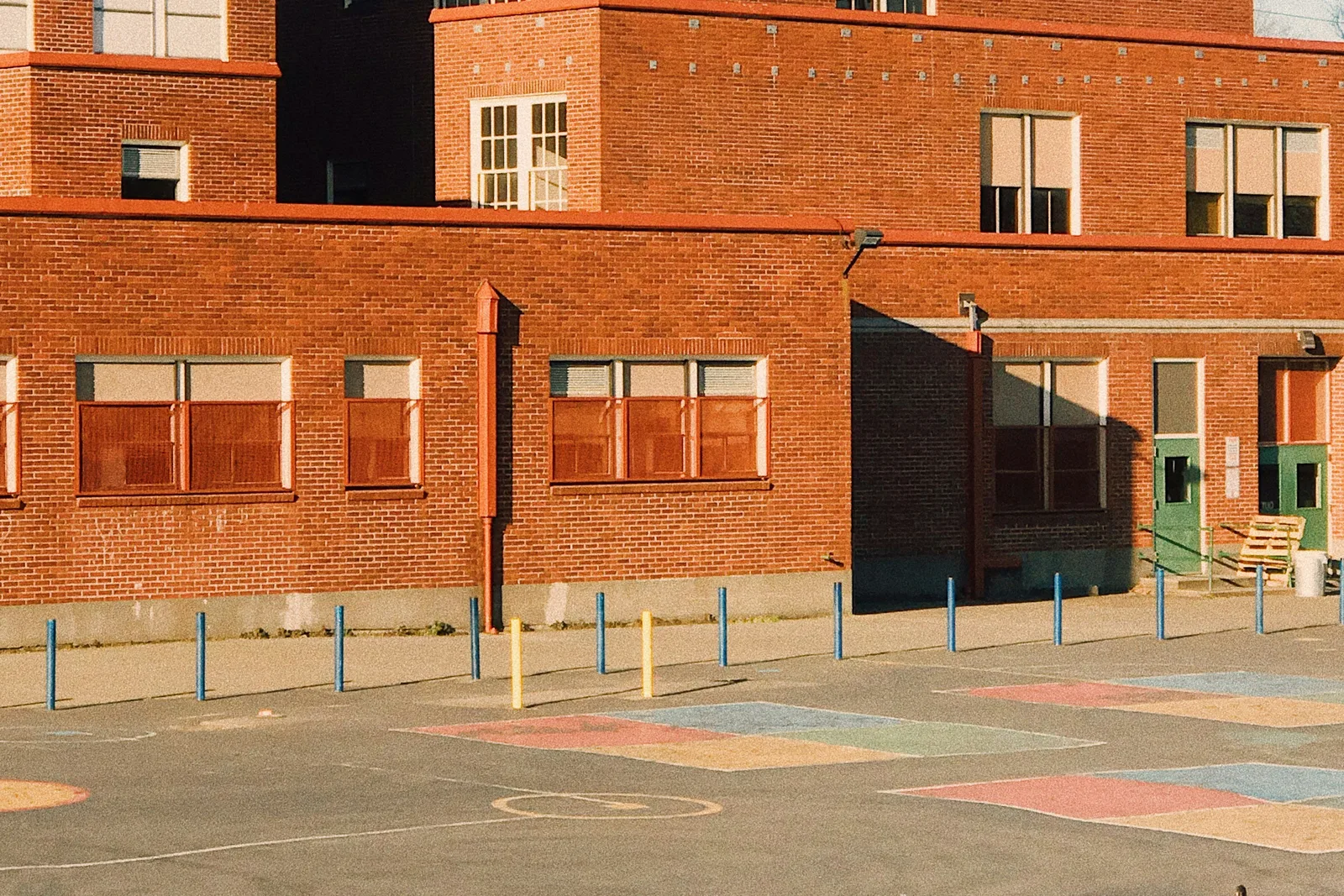 A red-brick school building above an empty playground painted with colored squares